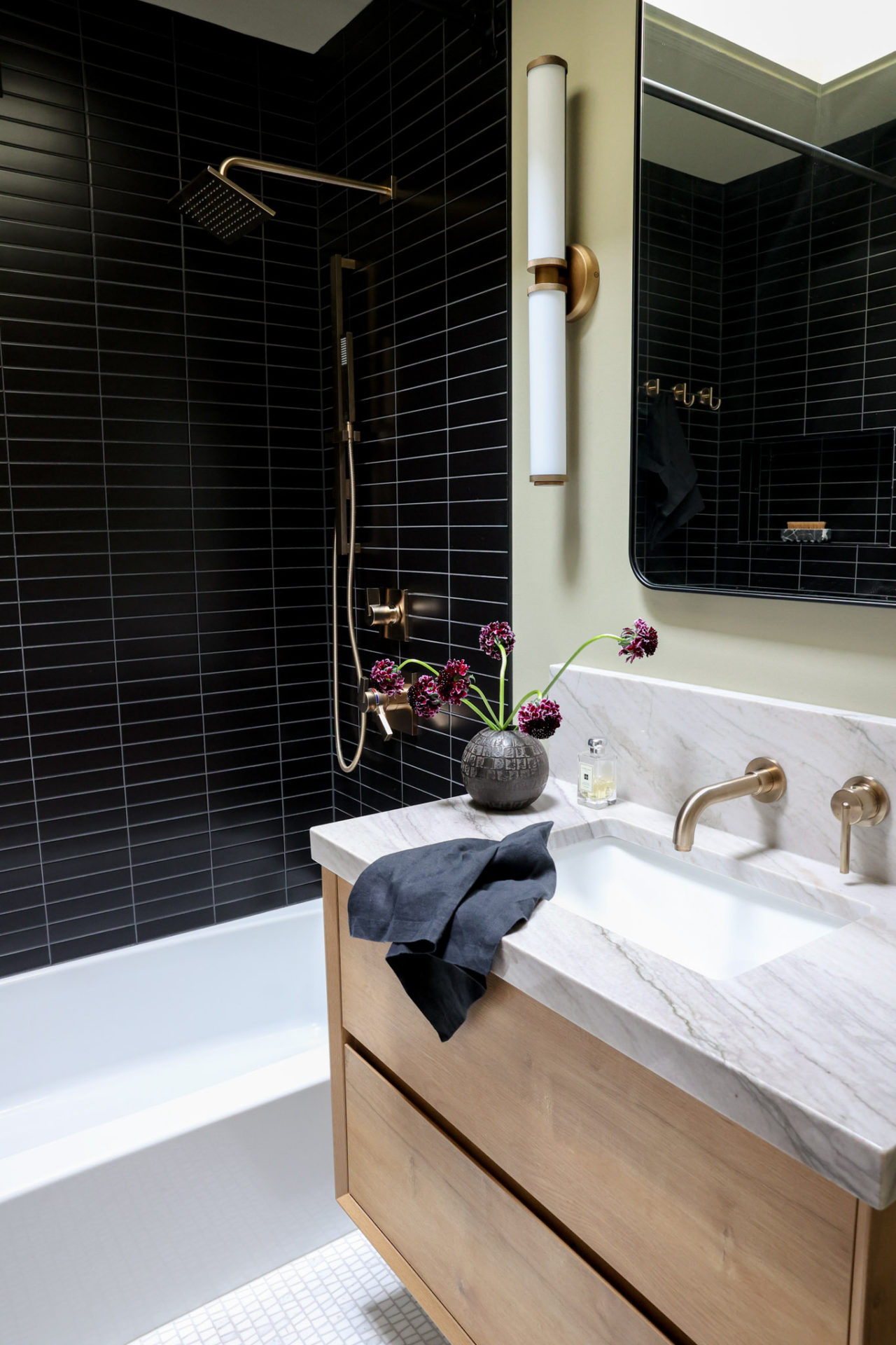 Floating vanity with wall mounted fixtures and black tiled shower in small bathroom, with champagne bronze Delta fixtures.