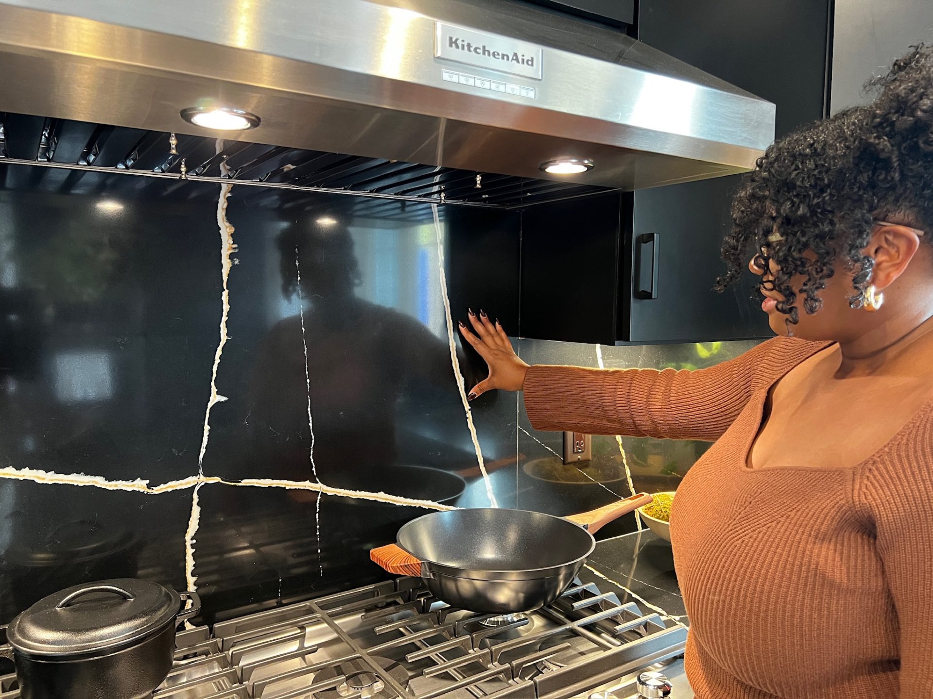 Rashida Banks showcasing a KitchenAid range hood over a black quartz backsplash and countertop.